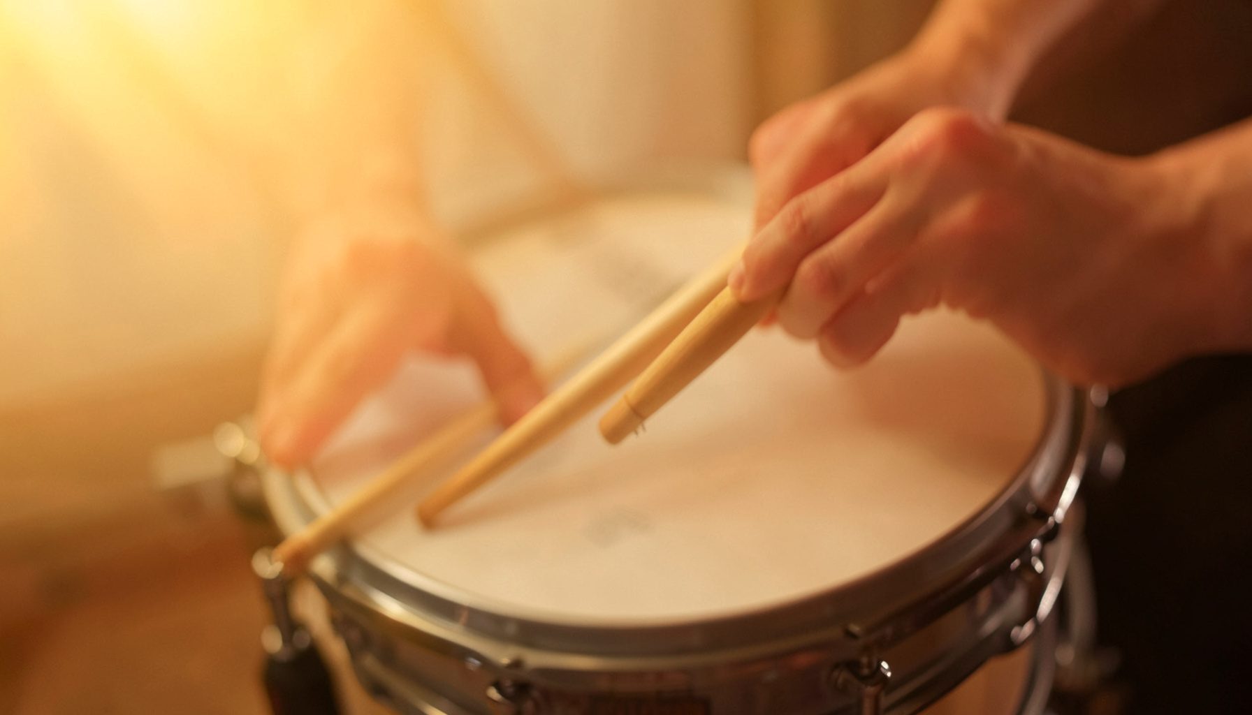 Close-up of hands and drumsticks over snare drum in warm golden light