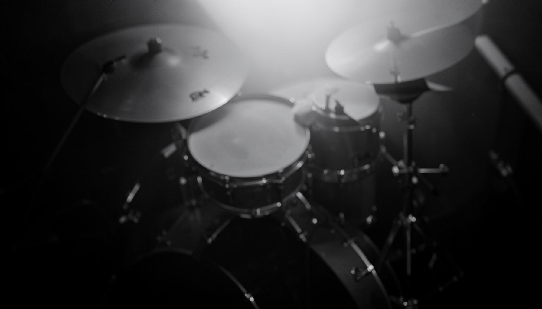 A moody black-and-white shot of cymbals and drum hardware in soft side light